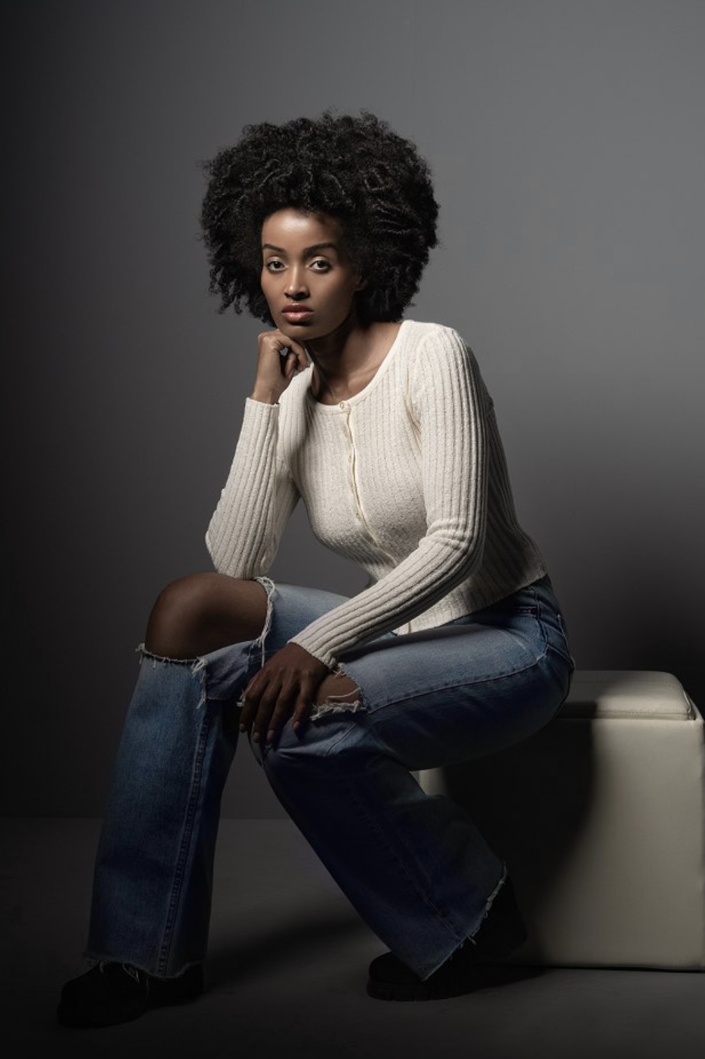Mimi seated in a cream knit and ripped denim jeans, studio editorial