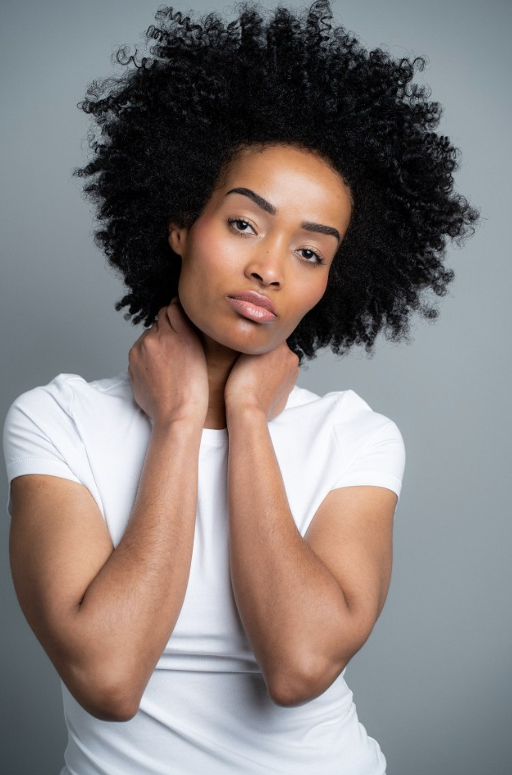 Mimi in a white t-shirt with hands resting at her neck, soft studio beauty portrait