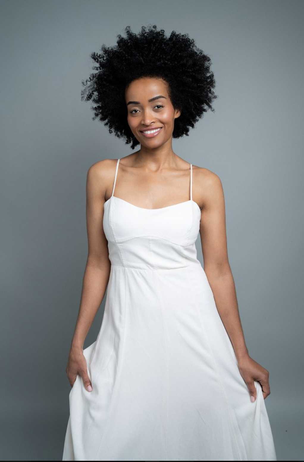 Mimi in a white slip dress smiling against a soft grey backdrop